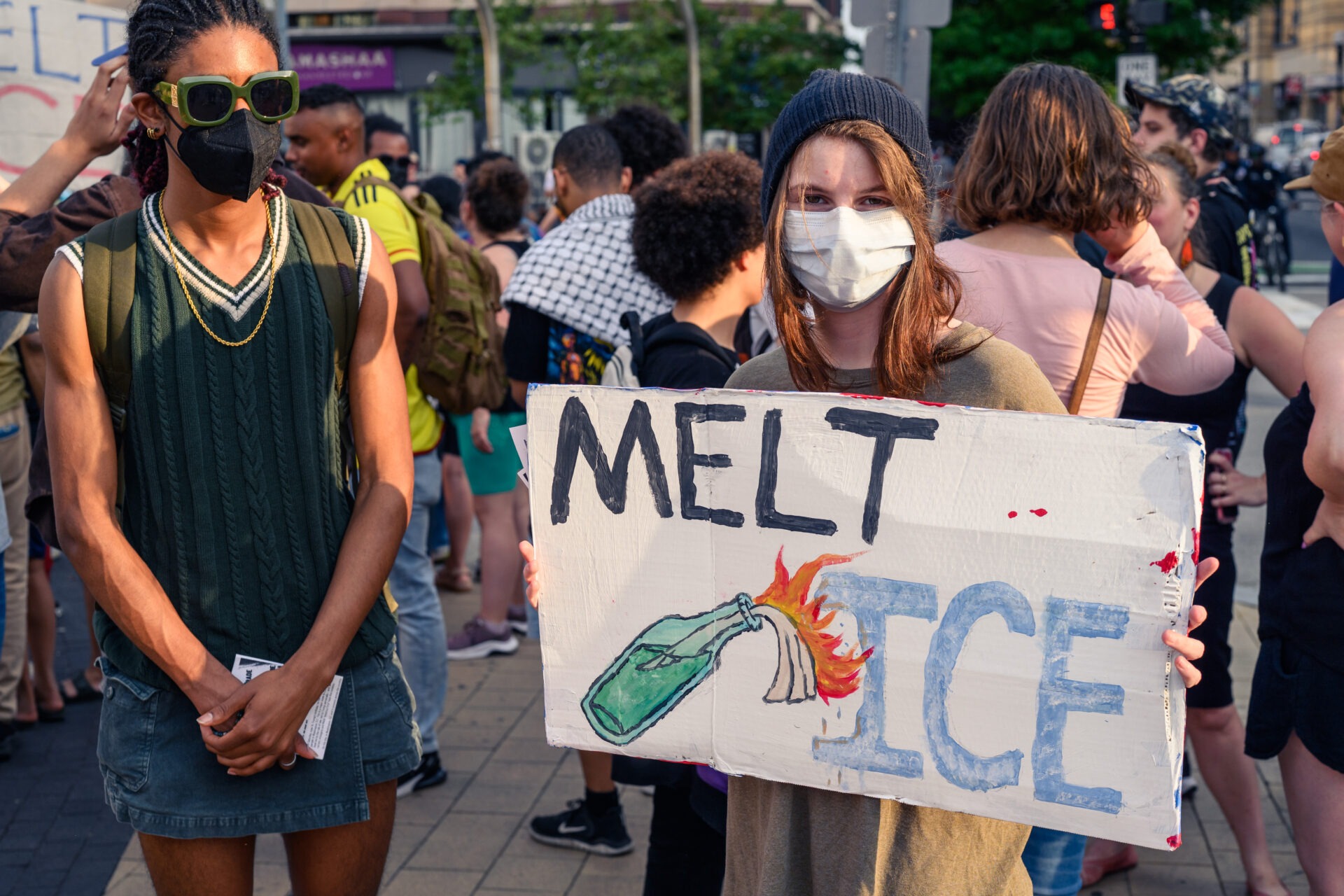 Two protestors are present at a protest against ICE in Washington DC, one is holding a poster that says 