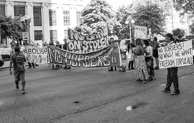 Black and white photo of ICE protestors marching with signs and banners.
