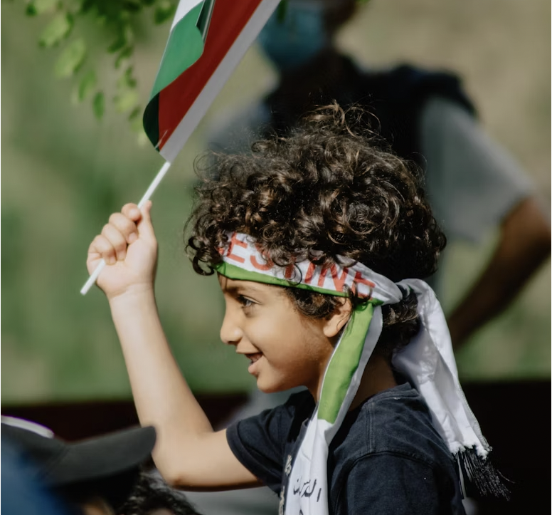 Young Palestinian boy smiles and holds up a Palestinian flag.