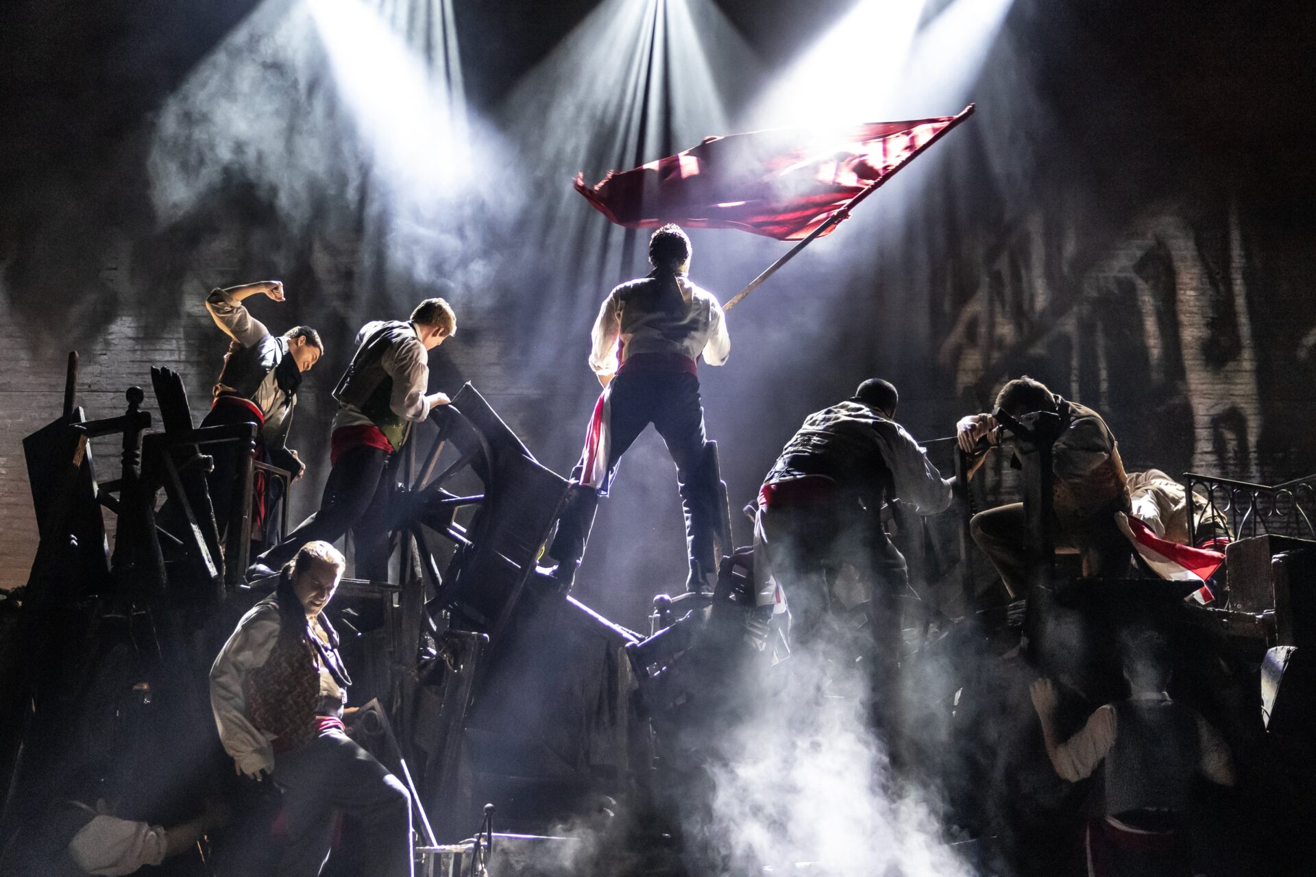A photograph of a 2024-2025 season performance of Les Misérables. Christian Mark Gibbs, reprising his role as Enjolras, is centered.