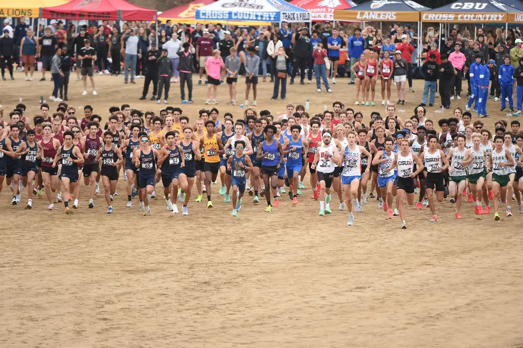 Multiple male runners run on a dirt path in front of pop-up tents