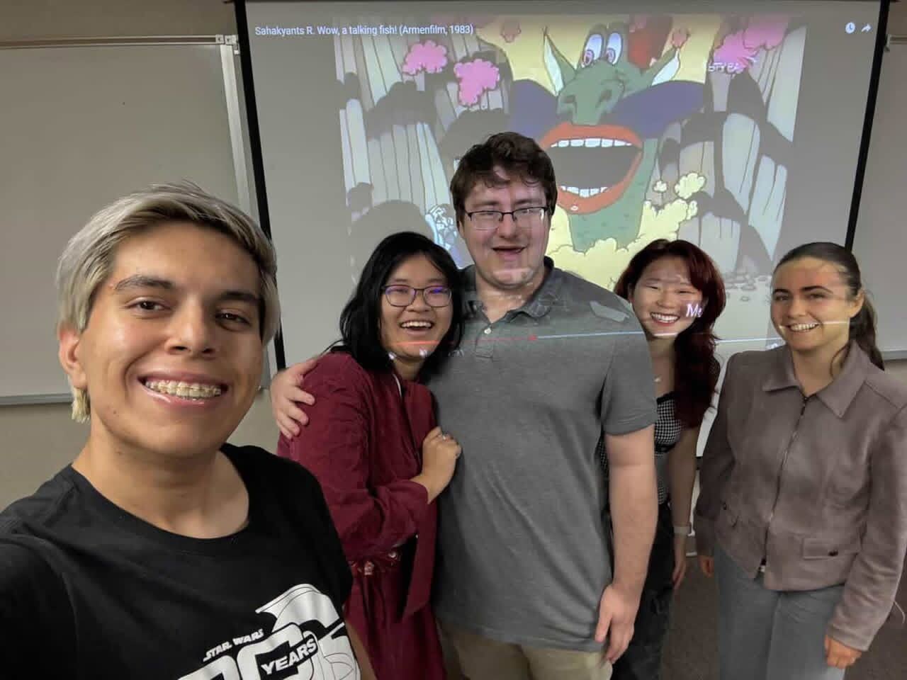 Five people from the UCI Russian club are shown in front of a projected screen of a movie playing.