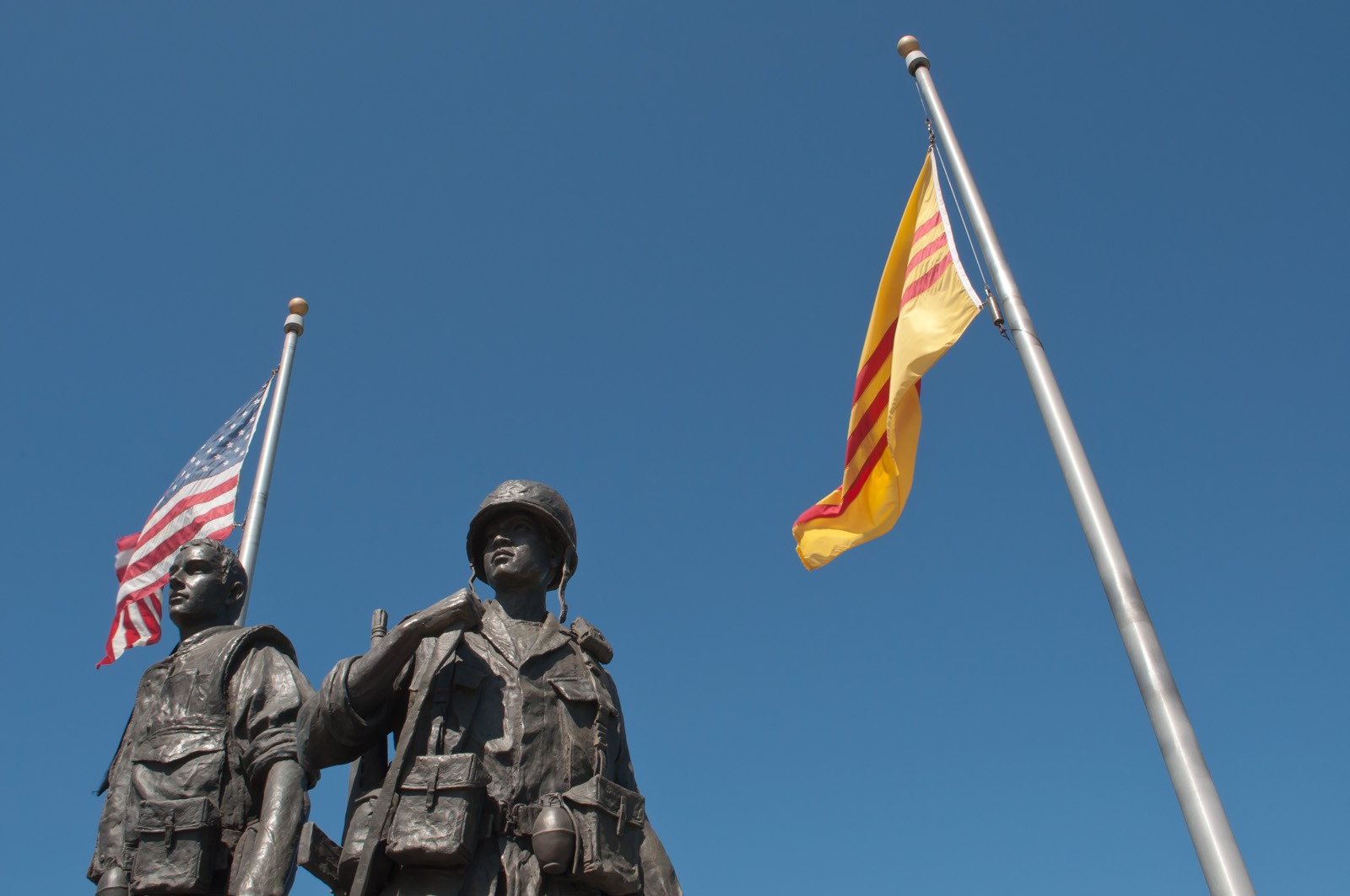 An American flag and South Vietnam flag are displayed behind two statues of soldiers.