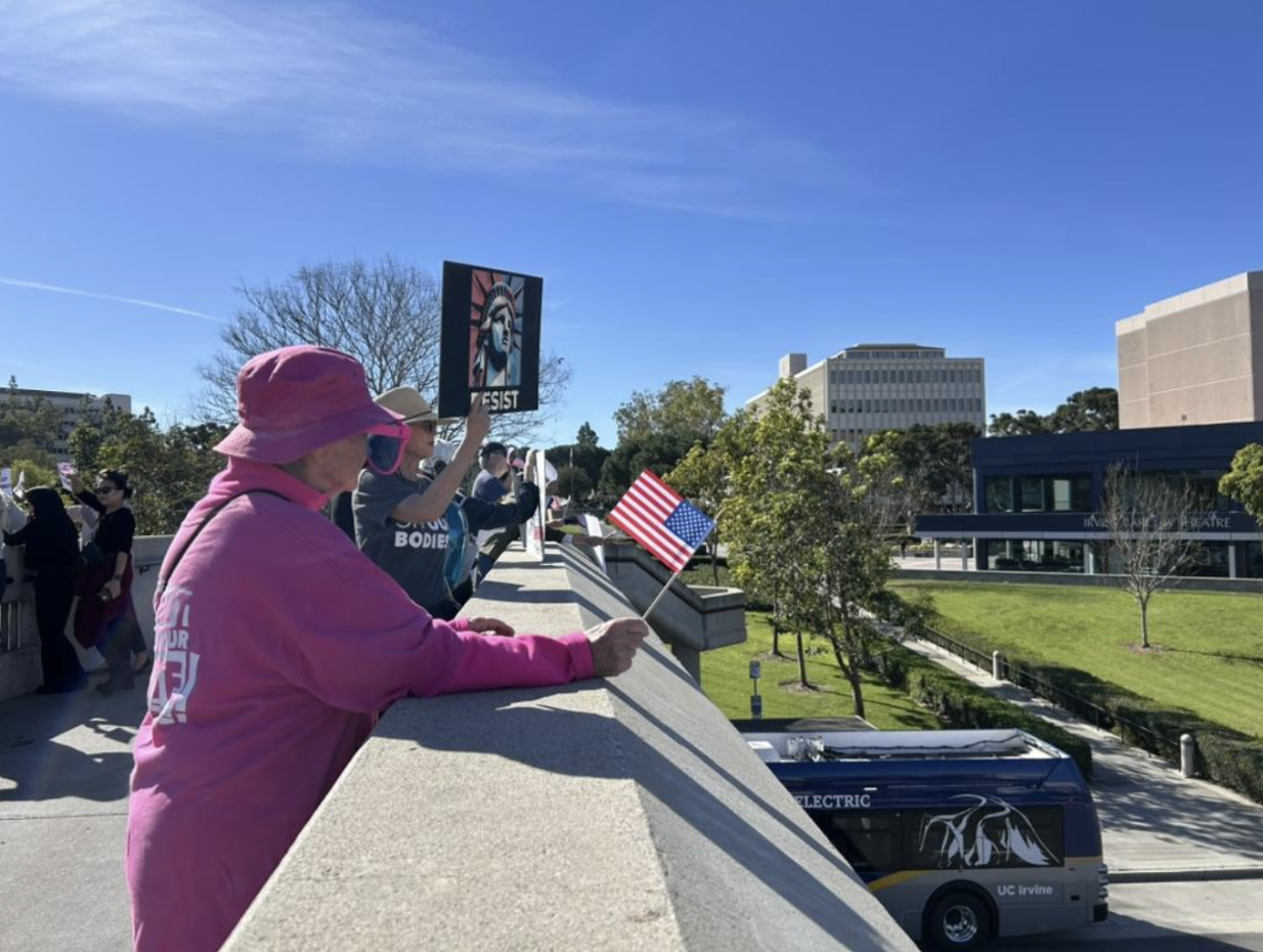 Photograph of a woman adorned in pink clothes standing and waving an American flag in Watson Bridge.