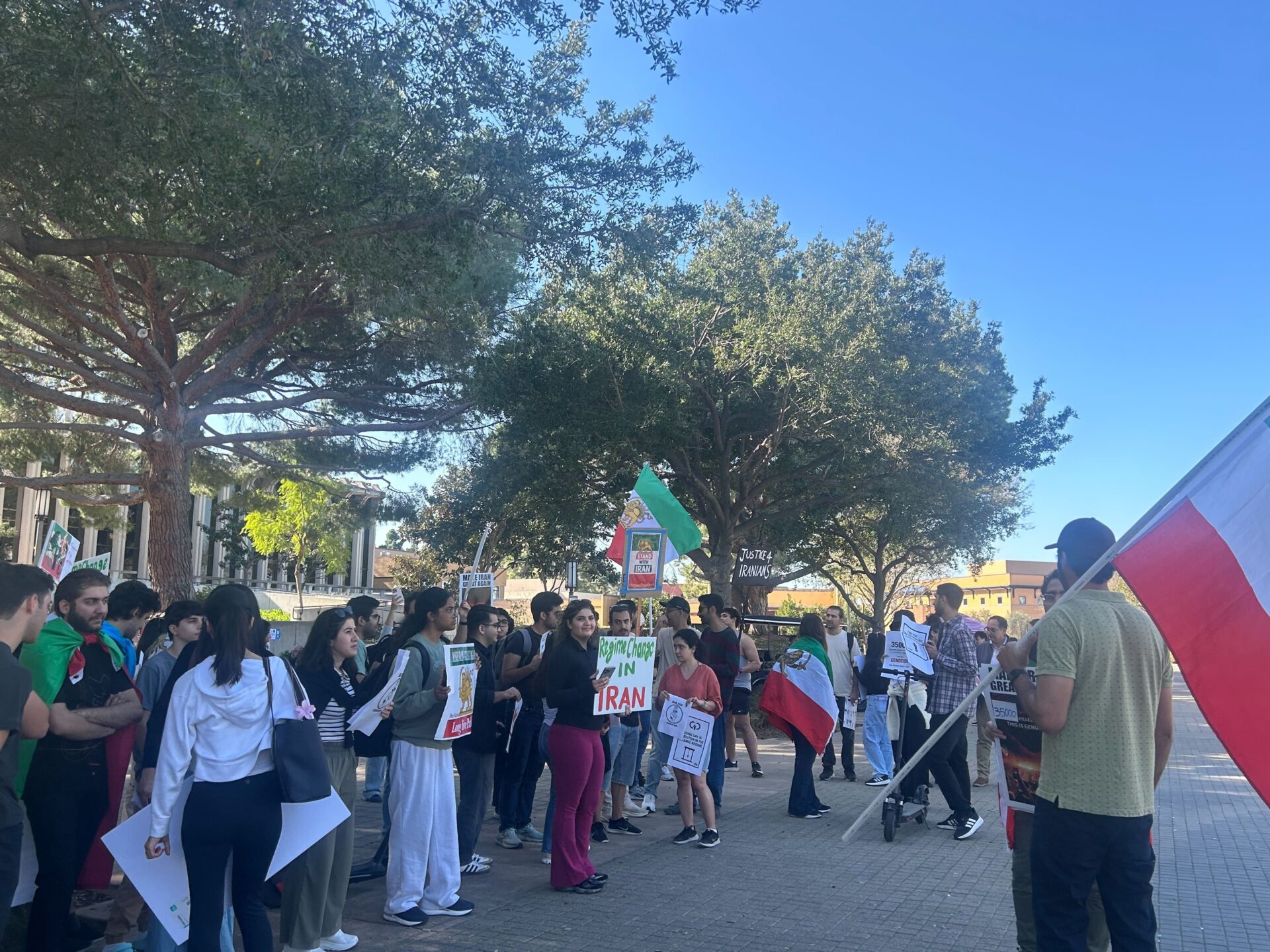Many students stand next to each other in a demonstration, carrying flags and signs. One sign reads 