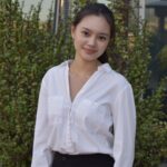 Deanza Andriansyah smiles in a white shirt in front of a bush