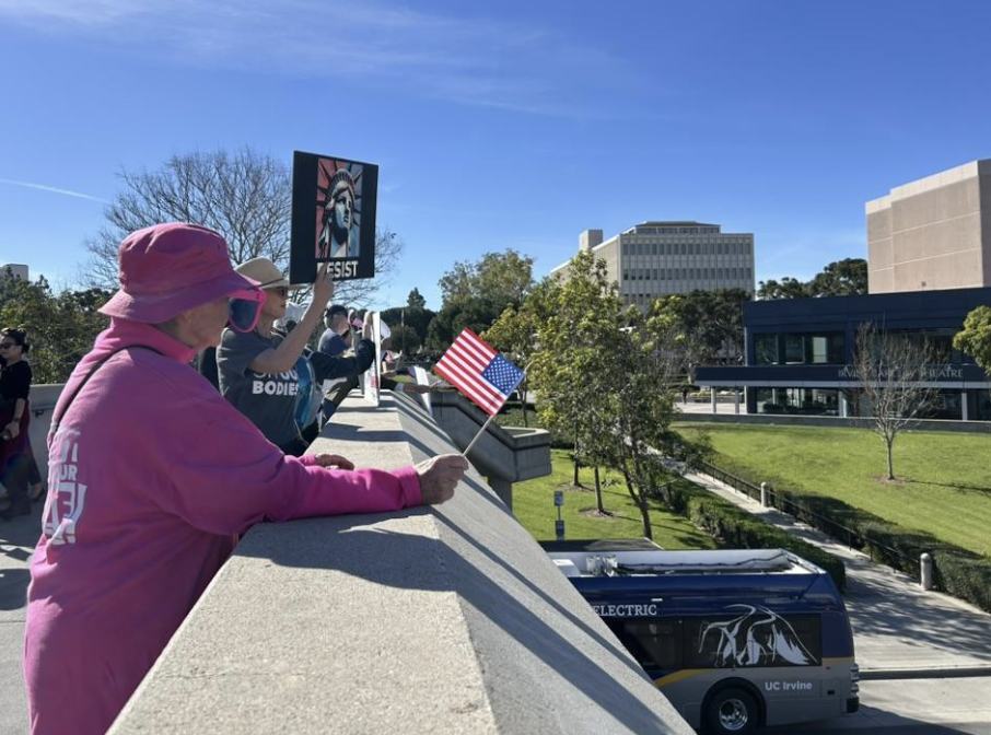 Protestor standing on Watson Bridge carrying a small American flag. Another holds up a sign that says 