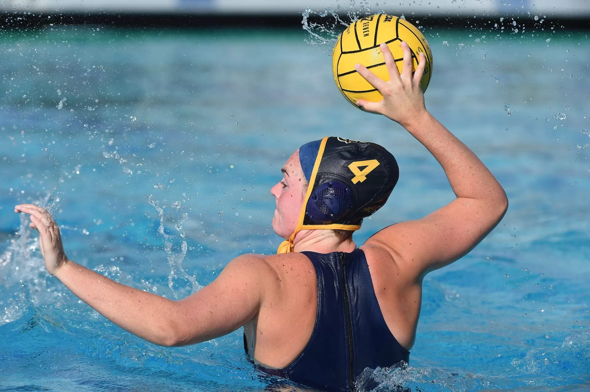Water polo athlete with a cap of number 4 holds a ball in an outdoor pool