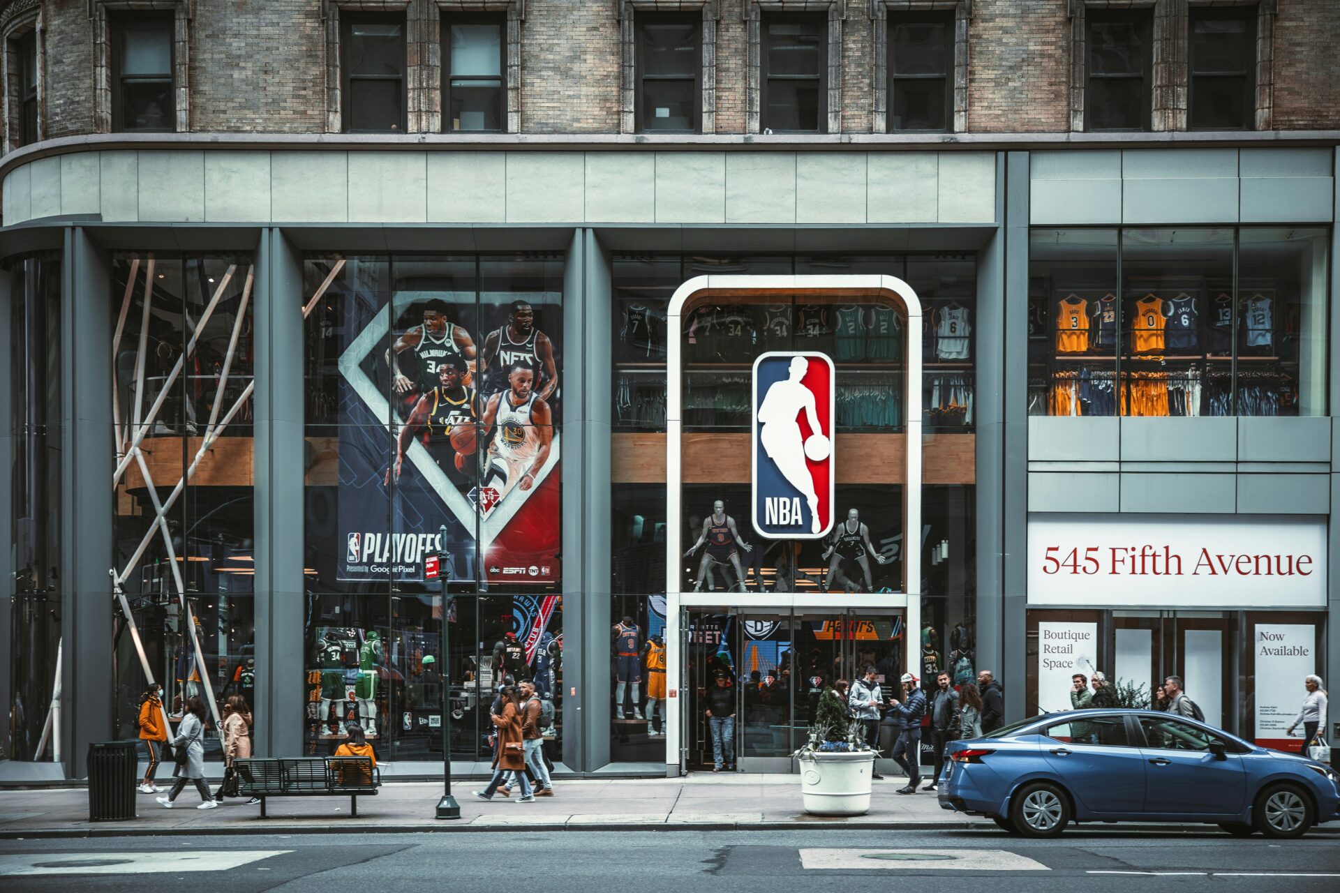 A glass-front NBA Store on Fifth Avenue features large playoff posters, rows of jerseys inside and an NBA logo above the entrance as pedestrians pass by on the sidewalk.