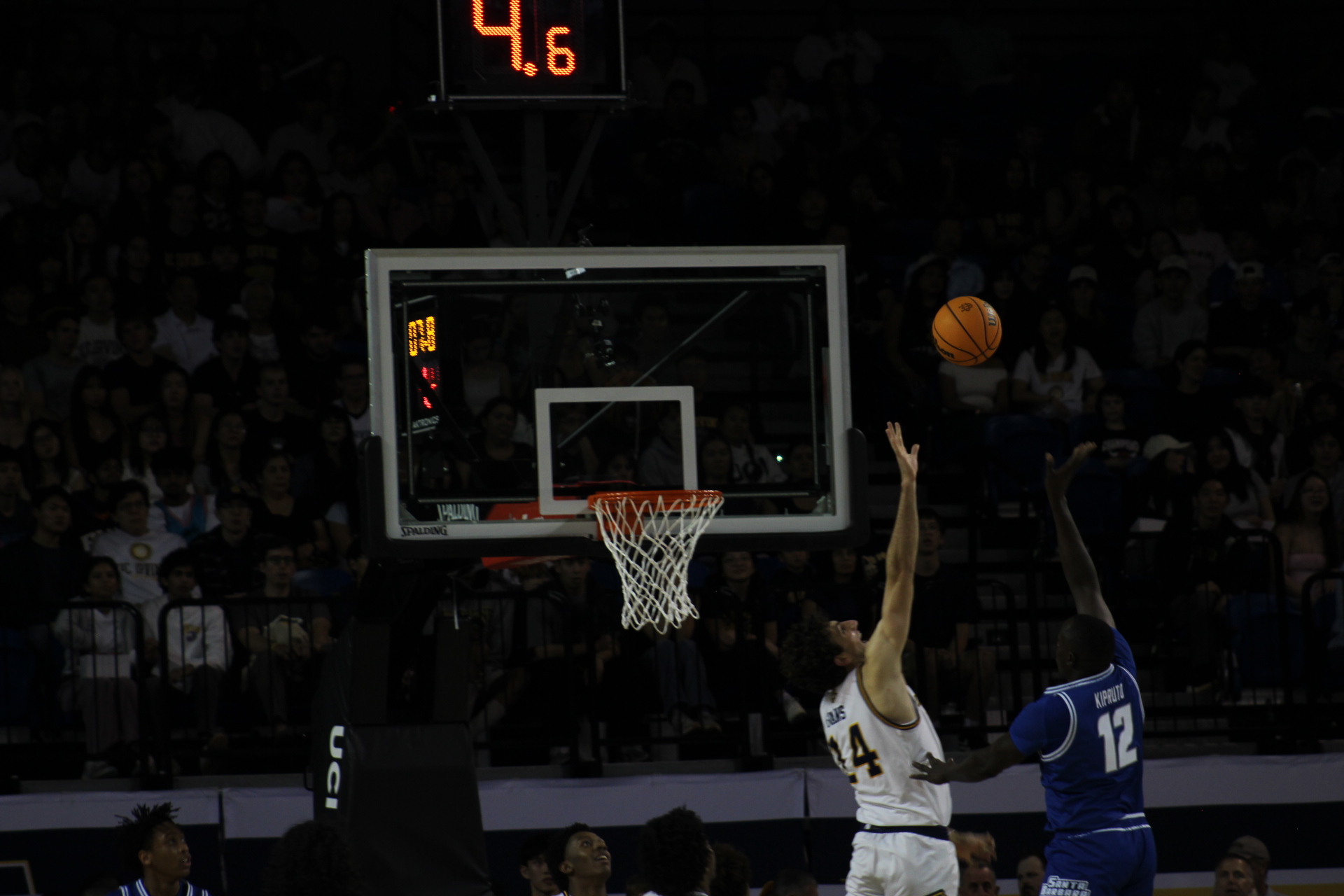 UCI's #14, Kyle Evans, leaps into the air, arm outstretched in attempting to block the UC Santa Barbara's shot from making it into the basket. They are close to the rim.