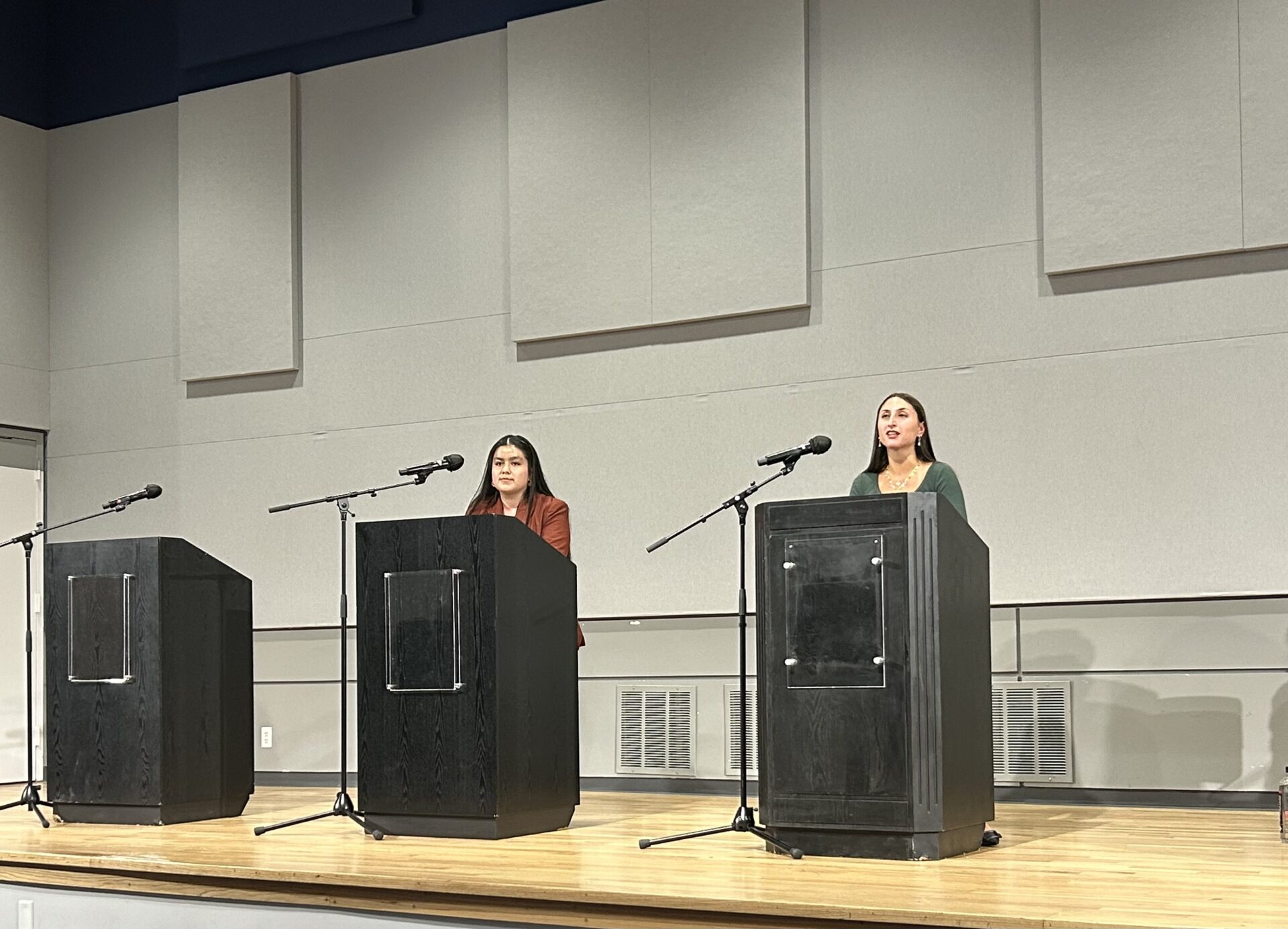 Two college students standing behind black podiums on a stage speaking into microphones.