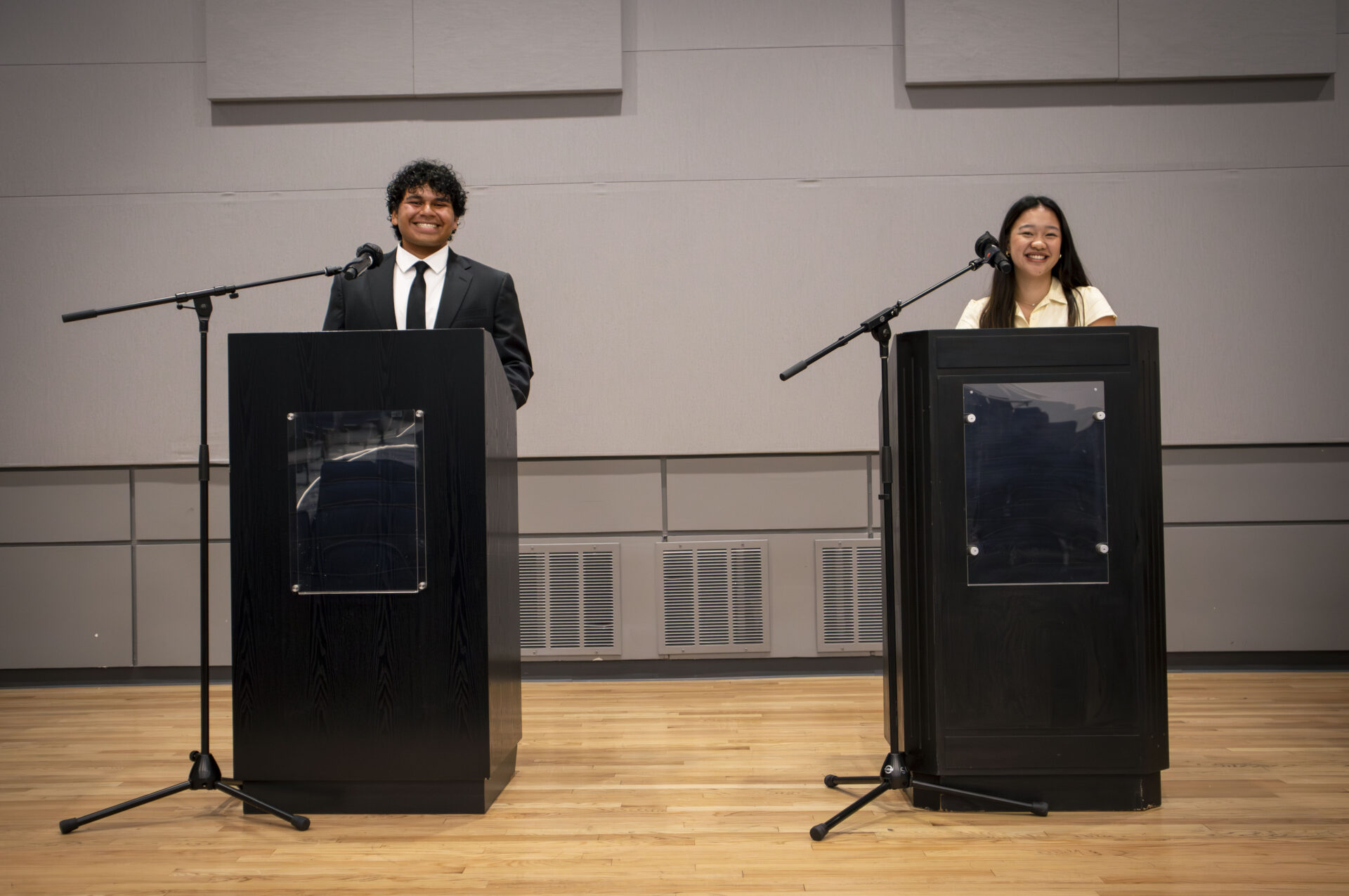 A young man and a young woman smile as they each stand behind their own podiums, side by side.
