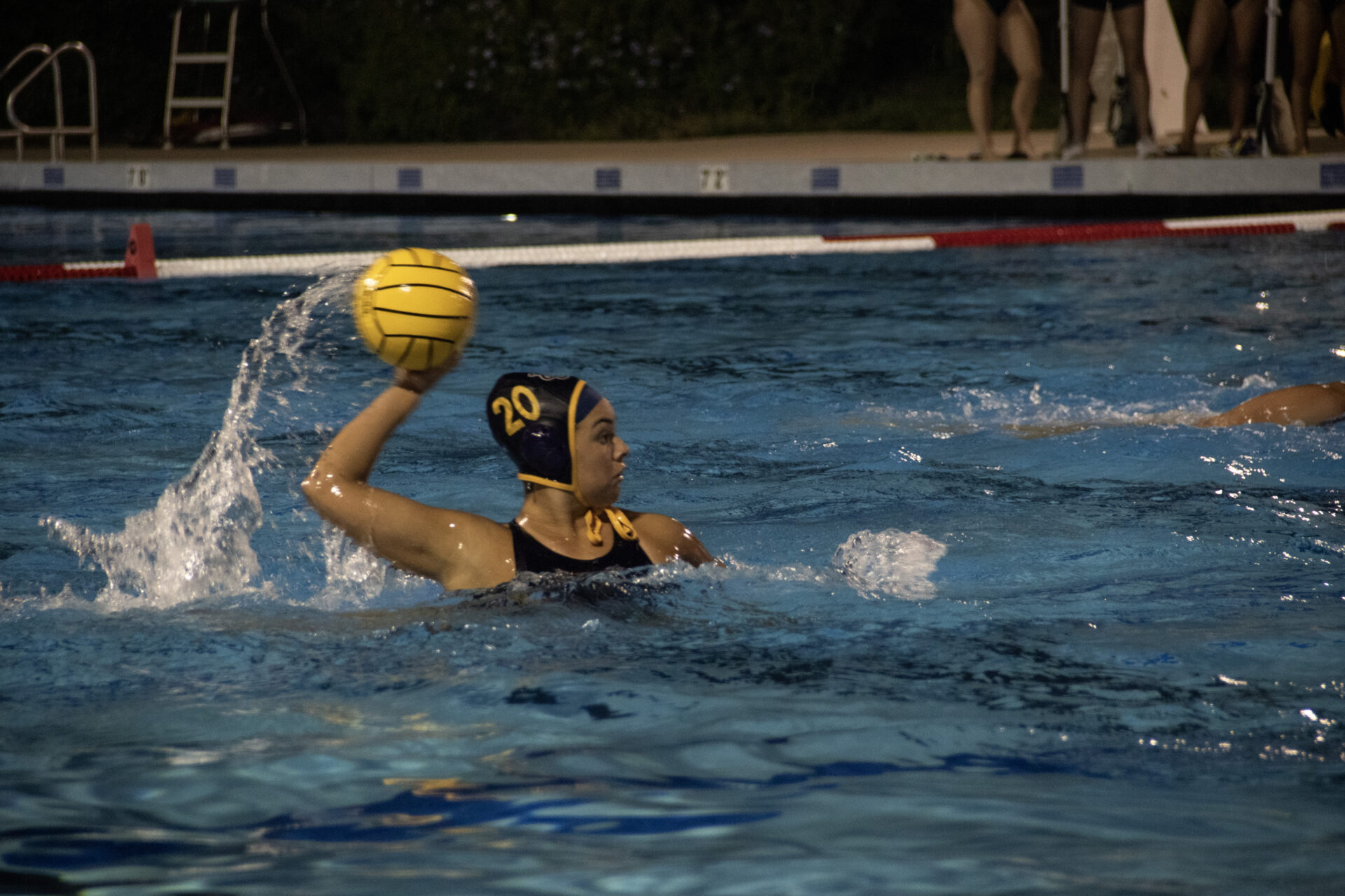 A UC Irvine women's water polo player lifts the ball above the water while swimming during a competitive match