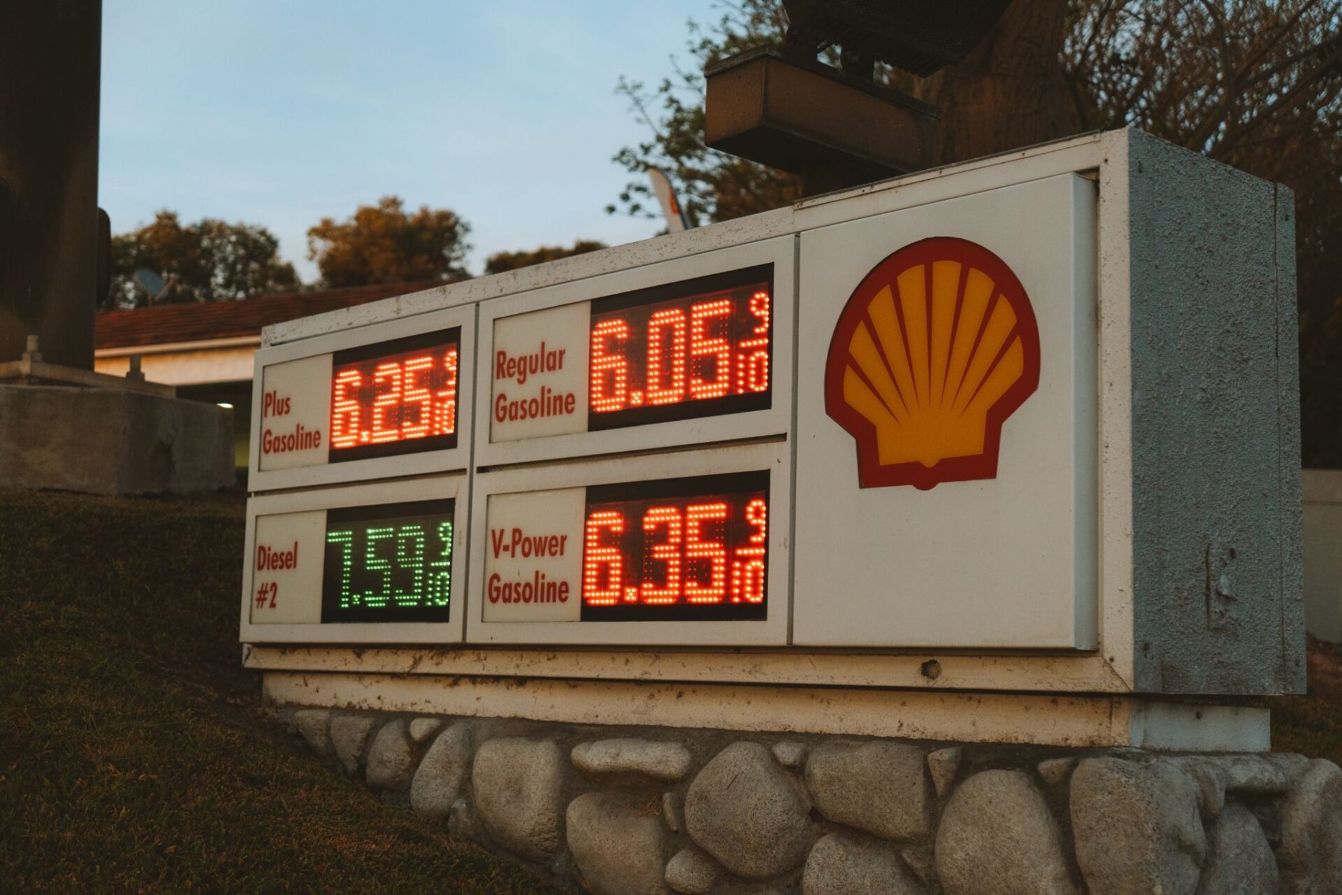 Shell gas station sign displaying prices with gas station in the background