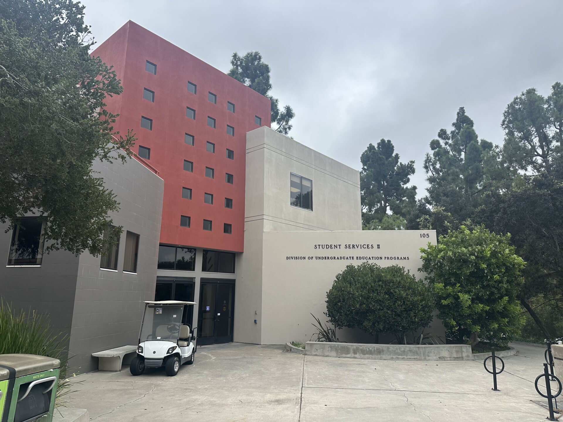 The outside of a building is shown on the left with trees and shrubs on the right.