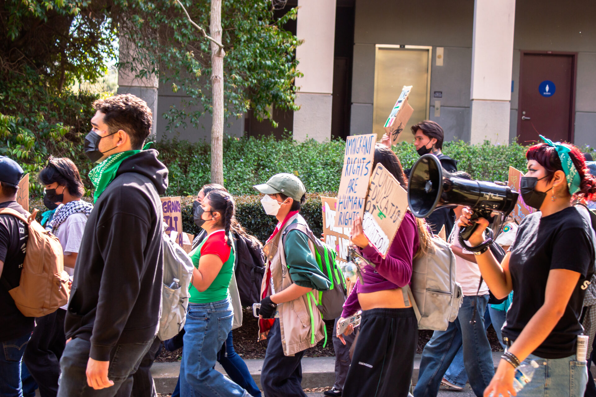 Photo shows pro-immigrant protestors walking in front of the UCI physical sciences building, holding signs.