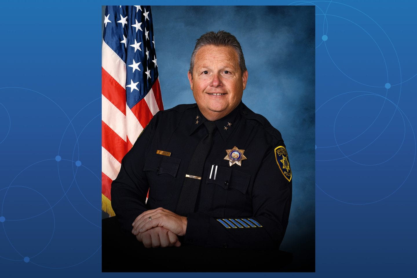 Portrait of Paul Cooper against a blue background. The American flag is shown on the left side of the frame.