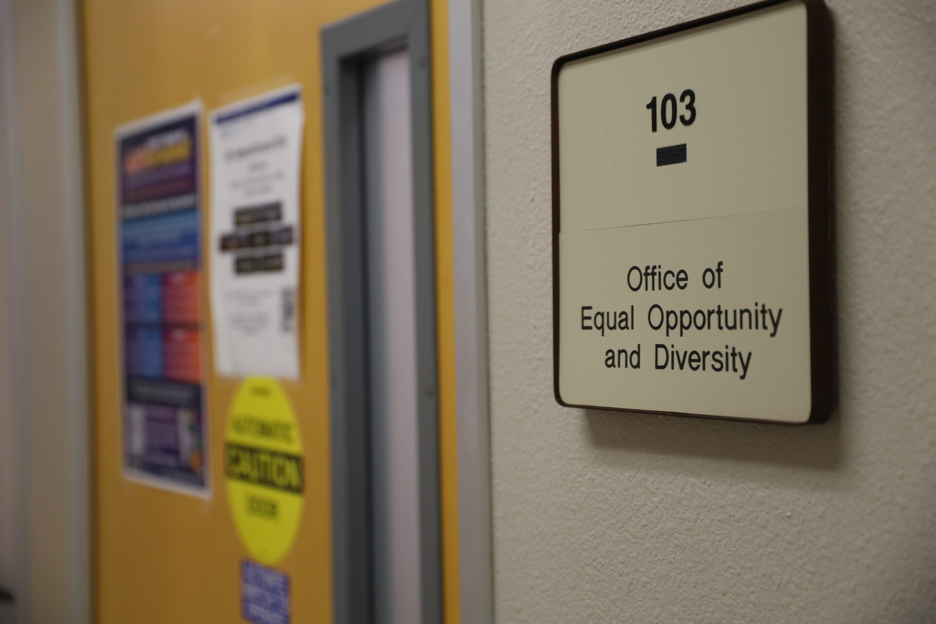 White wall plaque for the office of equal opportunity next to a door.