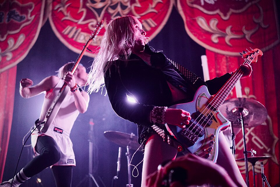 Two members of Frost Children on stage, playing guitar. One of them is jumping around energetically, while the other is standing tall.